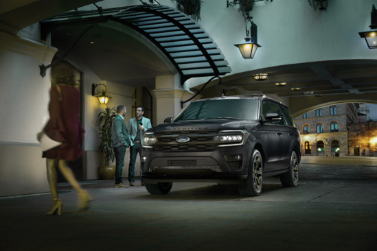 A sleek black SUV parked in an elegant, dimly lit urban setting. Two men converse nearby, while a woman in a red dress walks past, conveying sophistication.