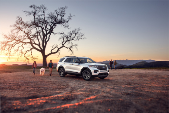 A white SUV is parked on a dirt path near a large leafless tree at sunset. People with children and a dog walk nearby, conveying a serene, outdoorsy vibe.